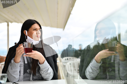 Image of woman in restaurant drinking tea wearing face mask