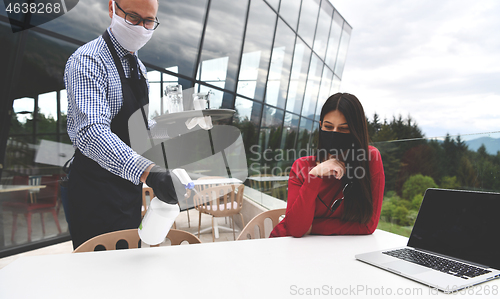 Image of Waiter with protective medical mask and gloves serving guest