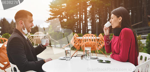 Image of couple with protective medical mask  having coffee break in a re