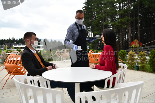 Image of Waiter with protective medical mask and gloves serving guest