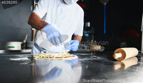 Image of chef  with protective coronavirus face mask preparing pizza