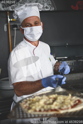 Image of chef  with protective coronavirus face mask preparing pizza