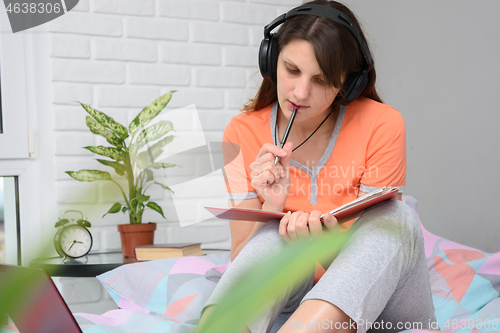 Image of Girl in home clothes and decor teaches lessons and listens to a lecture online.