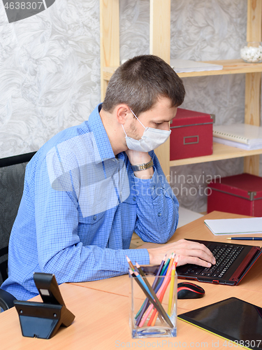 Image of An office worker sits at a desk wearing a medical mask