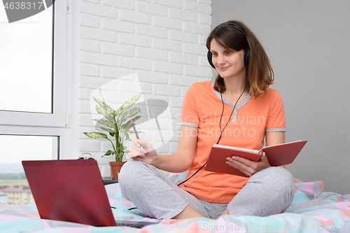 Image of Happy student in pajamas at home sitting on the bed in the bedroom is taking an interactive online training course