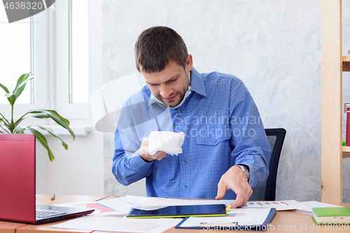 Image of A man in a blue shirt sits at a table in the office with a napkin in his hand