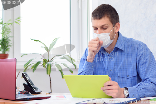 Image of sick office worker in medical mask sits at desk