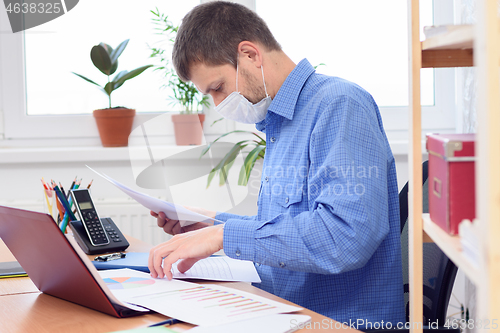 Image of office worker in medical mask disassembles documents on the desktop