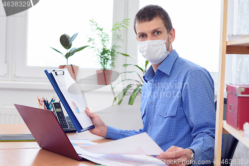 Image of Office worker in medical mask examines data in documents with amazement