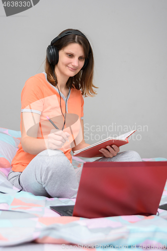 Image of Girl is studying online sitting at home in the bed in her pajamas and wearing headphones