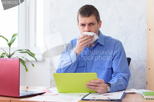 Image of An office worker with a tablet in his hand holds a napkin at his mouth