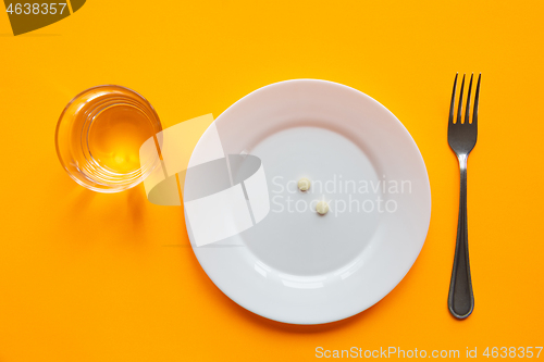 Image of On the plate is a handful of pills, next to it is a glass of water and a fork