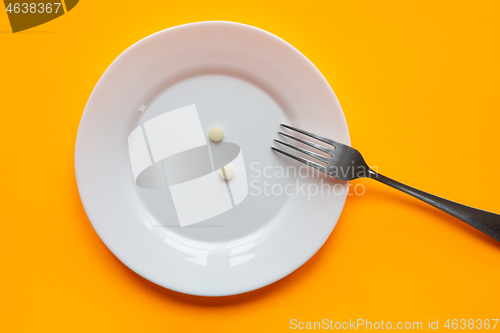 Image of On the plate are two tablets and a fork, orange background