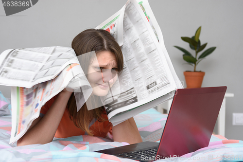 Image of Girl put newspapers to her head and looks at the laptop screen trying to find work