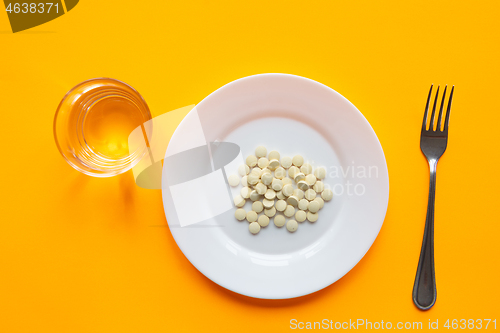 Image of On the plate are two tablets, next to it is a glass of water and a fork