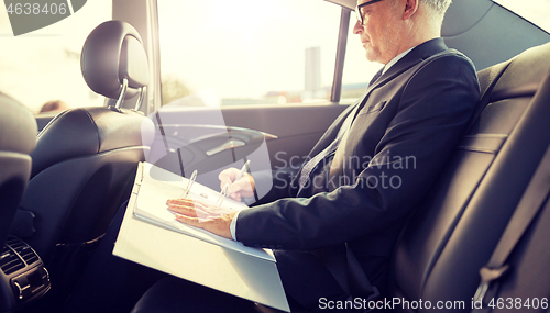 Image of senior businessman with papers driving in car