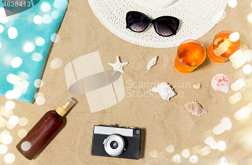 Image of drinks, hat, camera and sunglasses on beach sand