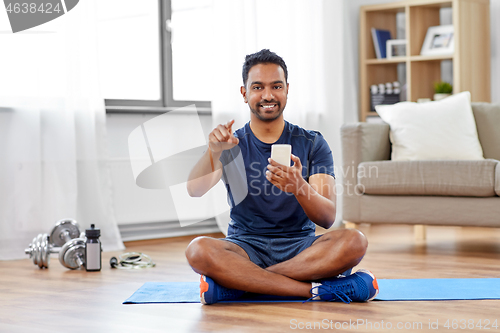 Image of indian man with smartphone on exercise mat at home