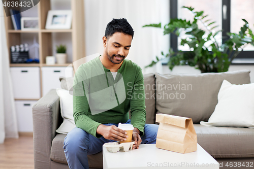 Image of indian man with takeaway coffee and food at home