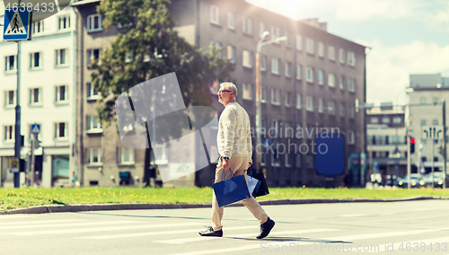 Image of senior man with shopping bags walking on crosswalk