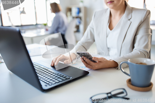 Image of businesswoman with smartphone and laptop at office