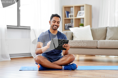 Image of indian man with tablet pc and exercise mat at home