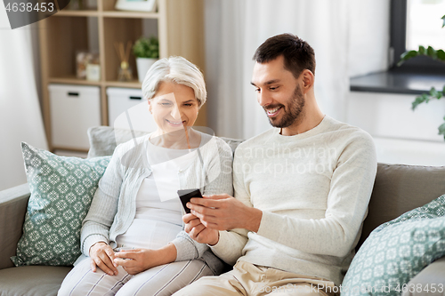 Image of old mother and adult son with smartphone at home