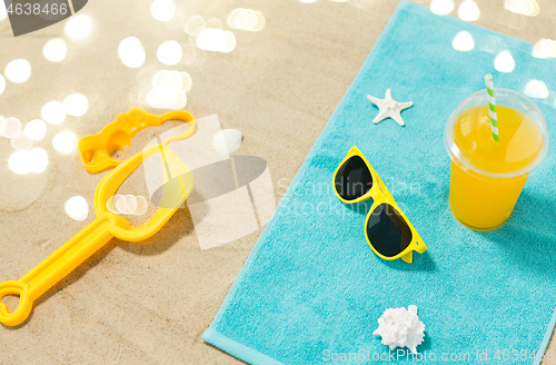 Image of sunglasses, sand toys and juice on beach towel