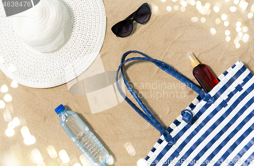 Image of beach bag, sunscreen, sunglasses and hat on sand