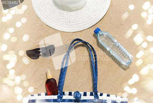 Image of beach bag, sunscreen, sunglasses and hat on sand