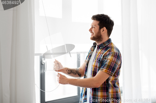 Image of man opening roller blind on window at home