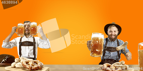 Image of Smiling men with beer dressed in traditional Austrian or Bavarian costume holding mug of beer at pub or studio. The celebration, oktoberfest, festival