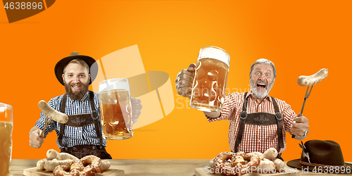 Image of Smiling men with beer dressed in traditional Austrian or Bavarian costume holding mug of beer at pub or studio. The celebration, oktoberfest, festival