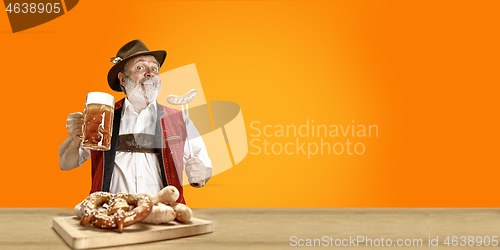 Image of Smiling senior man with beer dressed in traditional Austrian or Bavarian costume holding mug of beer at pub or studio. The celebration, oktoberfest, festival