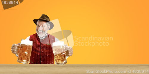 Image of Smiling senior man with beer dressed in traditional Austrian or Bavarian costume holding mug of beer at pub or studio. The celebration, oktoberfest, festival