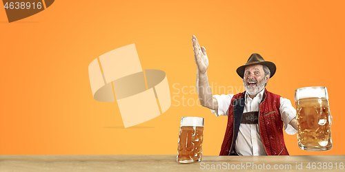 Image of Smiling senior man with beer dressed in traditional Austrian or Bavarian costume holding mug of beer at pub or studio. The celebration, oktoberfest, festival