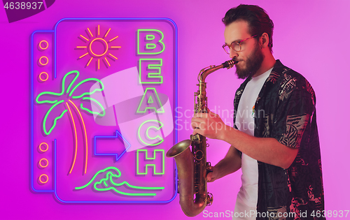 Image of Young jazz musician playing the saxophone in neon light with neon sign