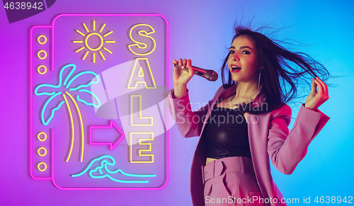 Image of Caucasian female singer portrait isolated on gradient studio background in neon light with neon sign