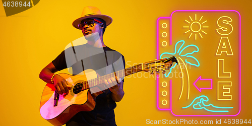 Image of Young musician playing guitar in neon light on gradient background, inspired, artwork