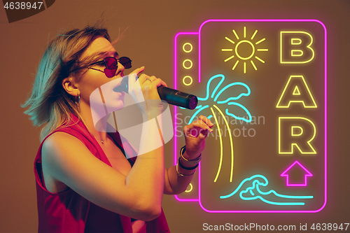 Image of Caucasian female singer portrait isolated on gradient studio background in neon light with neon sign