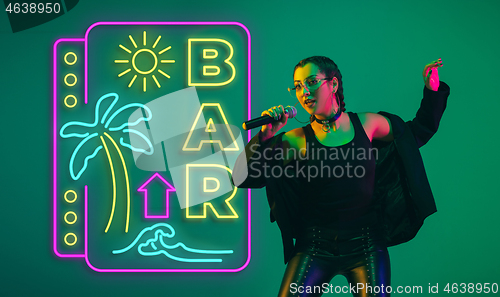 Image of Caucasian female singer portrait isolated on gradient studio background in neon light with neon sign