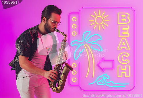 Image of Young jazz musician playing the saxophone in neon light with neon sign