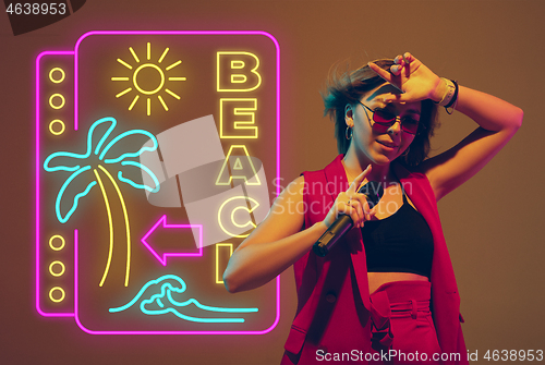 Image of Caucasian female singer portrait isolated on gradient studio background in neon light with neon sign