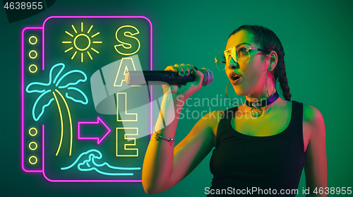 Image of Caucasian female singer portrait isolated on gradient studio background in neon light with neon sign