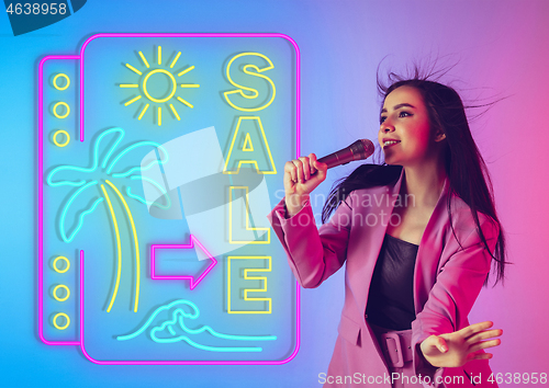Image of Caucasian female singer portrait isolated on gradient studio background in neon light with neon sign