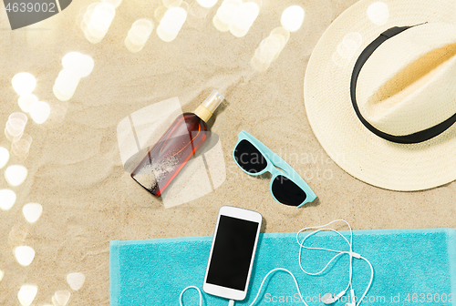 Image of smartphone, hat, flip flops and shades on beach