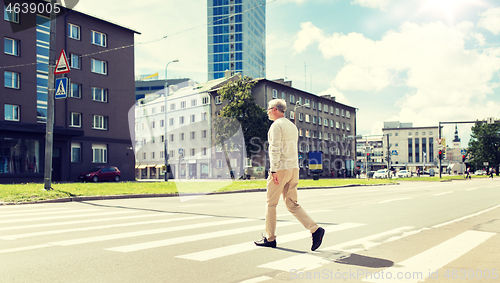 Image of senior man walking along city crosswalk