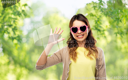 Image of asian woman in heart-shaped sunglasses waving hand