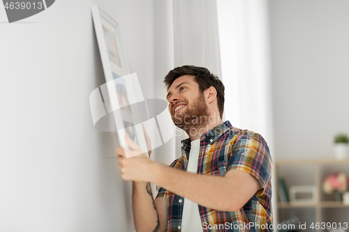 Image of man hanging picture in frame to wall at home