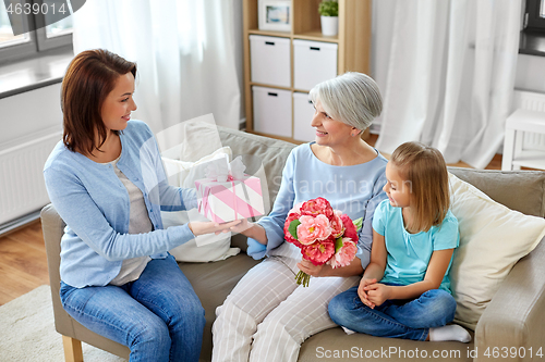 Image of family giving present and flowers to grandmother